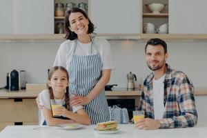 padre, madre e la loro piccola figlia amichevoli positivi sono di buon umore, trascorrono del tempo insieme, posano in cucina, si riuniscono per fare colazione, godersi l'atmosfera domestica e il giorno libero. ora di mangiare foto