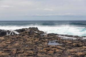 onde dell'oceano turbolente con schiuma bianca battono le pietre costiere foto