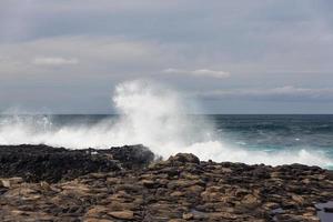 onde dell'oceano turbolente con schiuma bianca battono le pietre costiere foto