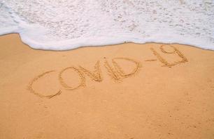 immagine del primo piano delle onde del mare che lavano la parola covid-19 dalla sabbia sulla spiaggia. concetto di fine pandemia foto
