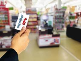 uomo d'affari in possesso di uno sconto della tessera del dieci percento sovrapposto al supermercato sfocato. foto