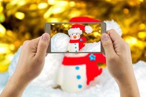 uomo che utilizza il telefono cellulare per guardare l'immagine ingrandita del pupazzo di neve con sfondo sfocato. celebrare il festival di natale felice anno nuovo foto