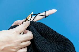 le mani della donna stanno facendo il cappello nero lavorando a maglia su sfondo azzurro foto