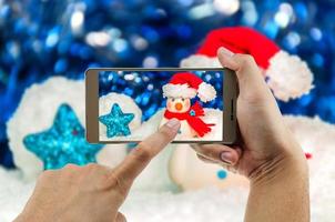 uomo che utilizza il telefono cellulare per guardare l'immagine ingrandita del pupazzo di neve con sfondo sfocato. celebrare il festival di natale felice anno nuovo foto