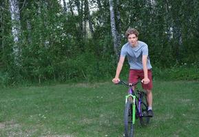 ragazzo adolescente in sella a una bicicletta in un parco. adolescente riccio in bicicletta. foto