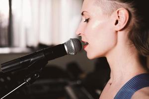 giovane cantante rock femminile con microfono, cantando. vista laterale. avvicinamento. donna con i capelli corti su un palco. spettacolo di musica dal vivo foto