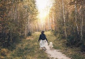 punto di vista posteriore della giovane donna che corre con il suo cane lungo un sentiero nella foresta. camminare con animali domestici, concetto di stare insieme. foto