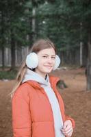 bella ragazza adolescente che indossa giacca rossa e cuffie che cammina nel parco. studentessa nella foresta. ragazza sorridente e guardando la fotocamera foto