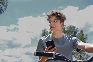 adolescente bello in sella a una bicicletta e in possesso di uno smartphone foto
