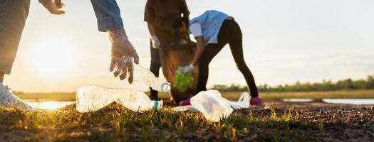 mano della donna che raccoglie la bottiglia di plastica dell'immondizia per la pulizia al parco foto