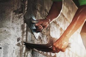 mano del primo piano del cemento intonacatura del lavoratore alla parete per la costruzione della casa foto