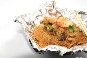 gamberetti al forno con spaghetti di vetro, un alimento tradizionale tailandese avvolto in carta freud trattata termicamente e bacchette, pronto da servire su uno sfondo bianco. foto