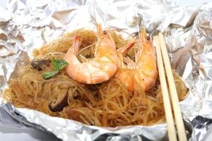 gamberetti al forno con spaghetti di vetro, un alimento tradizionale tailandese avvolto in carta freud trattata termicamente e bacchette, pronto da servire su uno sfondo bianco. foto