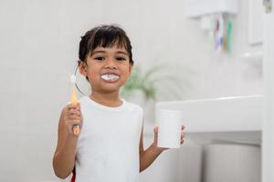 piccola neonata sveglia che si pulisce i denti con uno spazzolino da denti in bagno foto