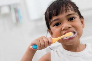 piccola neonata sveglia che si pulisce i denti con uno spazzolino da denti in bagno foto