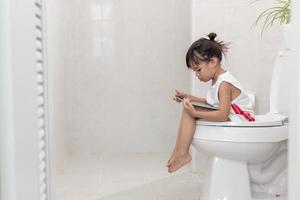 bambino seduto sul water che tiene il tablet.child addicted smartphone concept foto