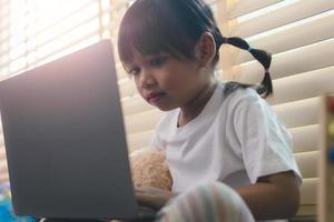 ragazza asiatica che utilizza un computer portatile per lo studio online homeschooling durante la quarantena domestica. homeschooling, studio online, quarantena domestica, apprendimento online, virus corona o concetto di tecnologia educativa foto