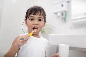 piccola neonata sveglia che si pulisce i denti con uno spazzolino da denti in bagno foto