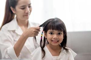 giovane madre asiatica che lega i capelli della figlia foto