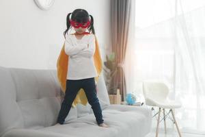 bambina in un costume da supereroe con maschera e mantello rosso a casa foto