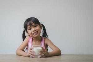 la bambina asiatica sta bevendo il latte da un bicchiere che era molto felice. foto