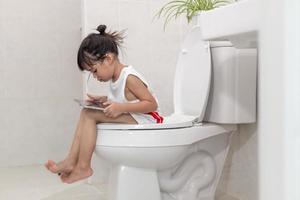 bambino seduto sul water che tiene il tablet.child addicted smartphone concept foto