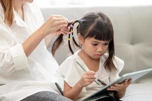 giovane madre asiatica che lega i capelli della figlia foto