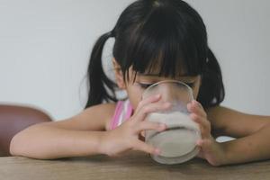 la bambina asiatica sta bevendo il latte da un bicchiere che era molto felice. foto