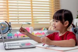 tempo di apprendimento. la scolaretta interessata con le cuffie si siede a casa e guarda la video lezione di istruzione. curiosa ragazza in età scolare pensa alla domanda dell'insegnante seleziona la risposta corretta sullo schermo del laptop foto