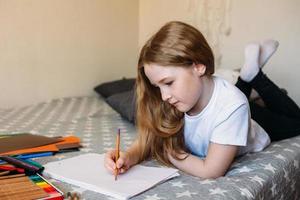 la ragazza dopo la scuola gioca a casa, disegna con matite e pennarelli foto