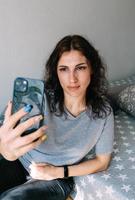 una giovane donna bruna sta riposando a casa e sta parlando su uno smartphone foto