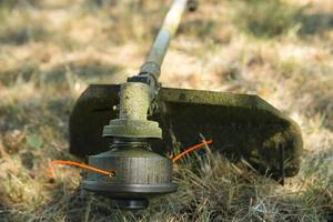 trimmer dopo aver falciato l'erba in primo piano. pompa benzina sull'erba con occhiali di sicurezza. abbellimento e abbellimento del terreno del giardino, cura del prato. foto