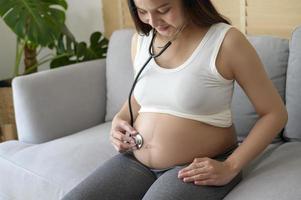 giovane donna incinta che mette lo stetoscopio sulla pancia, sull'assistenza sanitaria e sul concetto di cura della gravidanza foto
