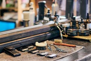strumenti per il taglio di capelli da barbiere attrezzatura da barbiere sul piano di lavoro in legno davanti allo specchio, vecchi interni vintage foto