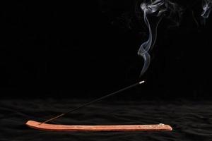 riccioli di fumo di bastoncino di incenso bruciato nel supporto di legno per il relax e la meditazione su sfondo nero foto
