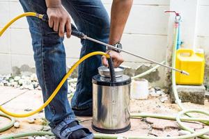 l'azienda asiatica del personale della termite della tailandia sta spruzzando il liquido chimico di distruzione nel nido di formiche bianche nel legno intorno alla casa umana. foto