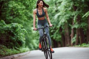 uno stile di vita sano. ciclista femminile su una bici su strada asfaltata nella foresta durante il giorno foto