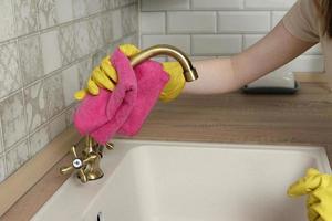 la donna in guanti pulisce il rubinetto con uno straccio. la donna pulisce la cucina foto