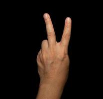 la mano dell'uomo che tiene due dita è un segno av, che significa vittoria. o ancora significa pace e disprezzo per le sfide su sfondo nero foto