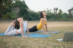 madre e figlia che fanno yoga. donna e bambino che si allenano nel parco. sport all'aperto. stile di vita sportivo sano, guardare esercizi di yoga tutorial video online e allungare il torace e la colonna vertebrale. foto