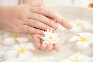 trattamento termale e prodotto per piedi femminili e spa per le mani. fiori bianchi in ciotola di ceramica con acqua per l'aromaterapia alla spa. foto