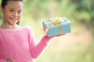 ritratto di natale di bambina sorridente felice con confezione regalo vicino a un albero di ramo verde. foglie verdi bokeh sfocato sfondo dalla foresta naturale. foto