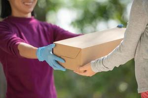 donna asiatica del servizio di consegna in t-shirt viola, ritratto di uomo di consegna tiene il pacco di cartone in piedi con il cliente davanti alla porta di casa. concetto di acquisto con consegna a domicilio. foto