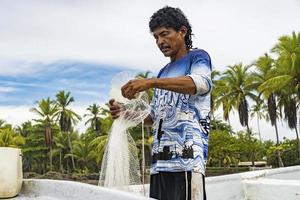 pescatore che prepara la sua rete sulla riva con palme sullo sfondo. foto