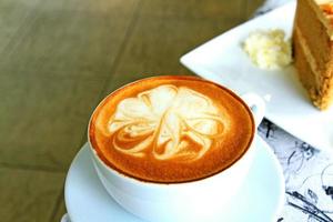 tazza di caffè cappuccino caldo sul tavolo con torta sfocata e sfondo panna montata foto