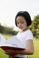 la bambina asiatica apre un libro nel parco foto