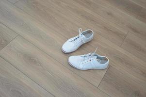 scarpe converse bianche per camminare, camminare, in piedi su un pavimento di legno marrone. adesivo anti mais sul retro del tallone. foto
