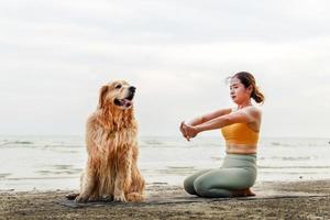 donna esercizi di yoga sulla spiaggia con il suo simpatico cane. concetto di stile di vita attivo sano. relax con un animale domestico. foto