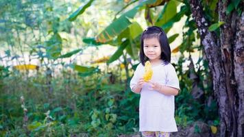 ragazza asiatica del bambino che tiene la farina croccante profonda della zucca fritta, cibo tradizionale birmano. dolce sorriso bambino che guarda l'obbiettivo. i bambini provano cibo sconosciuto. il bambino indossa magliette bianche. spazio vuoto per inserire il testo foto