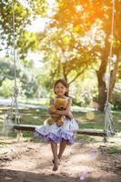 bambina carina seduta altalene, orsacchiotto seduto con lei, bambina indicò l'albero. foto